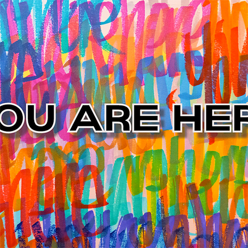 The words “you are here” are handwritten over and over again in different colors, slightly overlapping each other. Over the top, “You Are Here” is printed in all-caps using a bold, black text with a white outline and drop shadow.