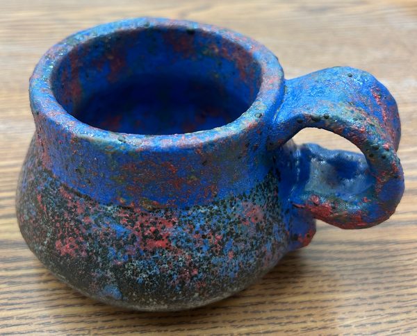Photo of a ceramic mug. The top inch, interior, and handle are glazed blue, while the bottom exterior is speckled blue and red, revealing the gray ceramic body beneath.