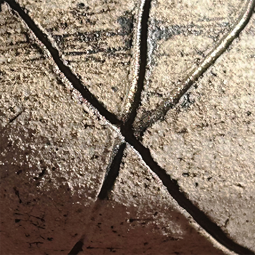 Closeup of five lines carved into a ceramic piece and converging at a center point to create the impression of a star. A black glaze was applied and wiped off before firing, leaving dark streaks on the surface and within the lines.