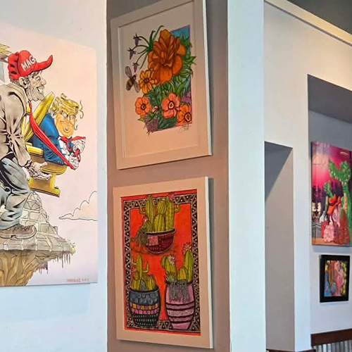 A photograph of various works of art hanging on gray walls, depicting President Trump, flowers, cactuses, and an alligator.