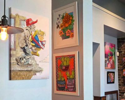A photograph of various works of art hanging on gray walls, depicting President Trump, flowers, cactuses, and an alligator.
