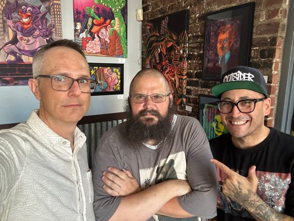 Photograph of Sacramento-based artists Jesse Baggs, Gabriel Sanford, and Tony Allen standing in front of various works of art by Baggs for the August, 2026 You Are Here art show at Weatherstone.