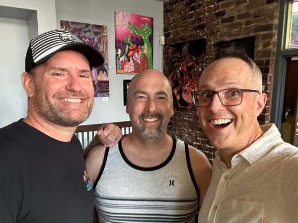 Photograph of Sacramento-based artist Jesse Baggs and his friends Wesley and Adam standing in front of various works of art by Baggs for the August, 2026 You Are Here art show at Weatherstone.